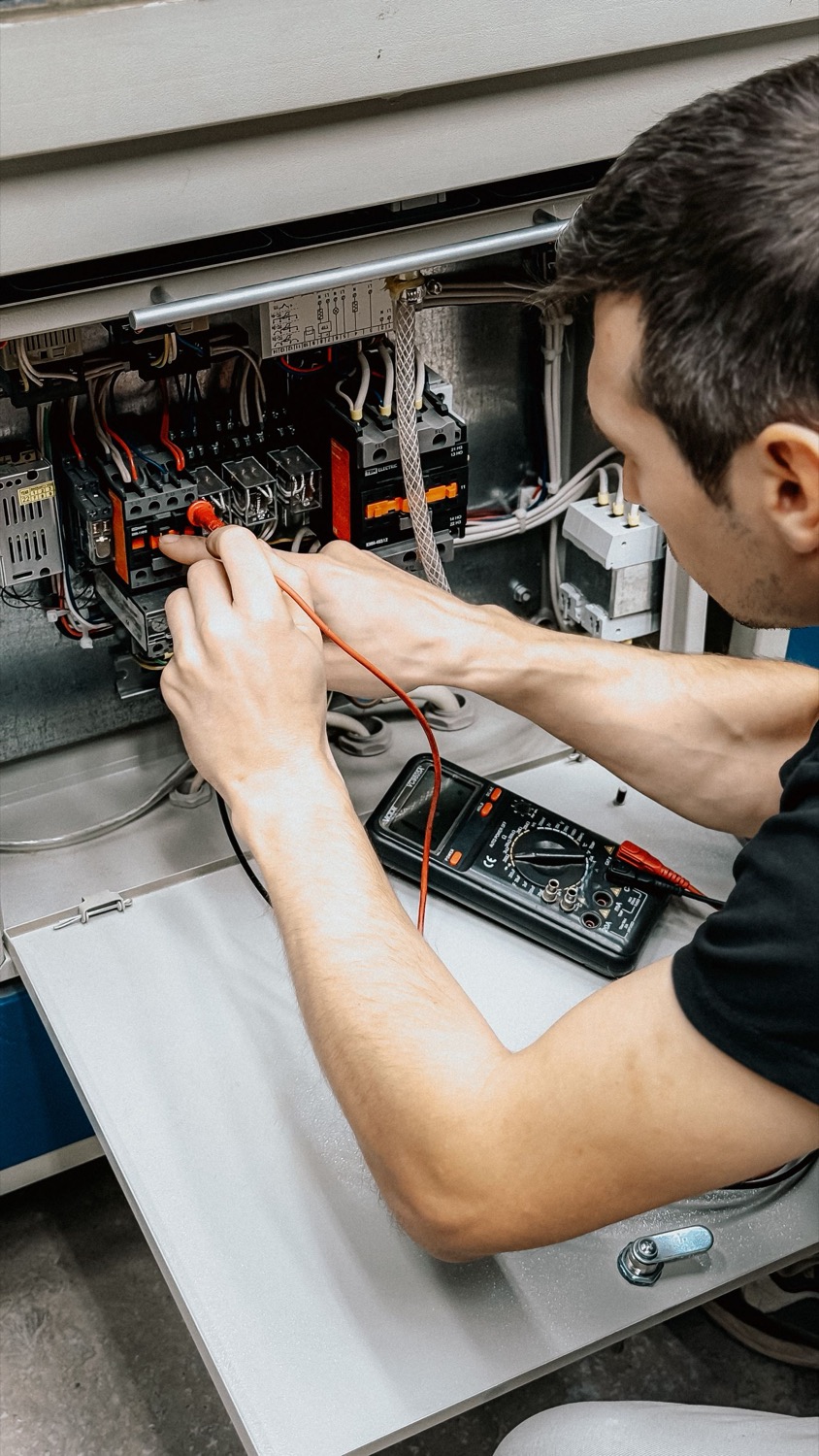 An electrician testing wiring in an electrical control panel with a multimeter